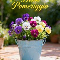 Vaso azzurro con viole multicolori su pavimento in terrazza, sullo sfondo verde sfocato