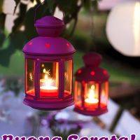 Lanterne colorate con candele accese appese in un giardino serale