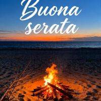 Falò sulla spiaggia al tramonto, mare calmo e cielo blu-arancio con scritta di augurio