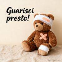 Orsacchiotto con bende e cerotti, seduto su un letto, con scritta di augurio di pronta guarigione