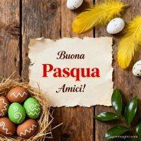 Biglietto di auguri pasquali su legno con uova decorate, piume gialle e foglie verdi