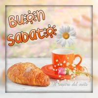 Colazione con cornetto e tazza arancione su sfondo floreale. 'Buon Sabato' è scritto sopra