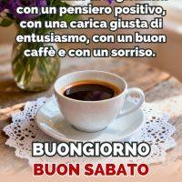 Tazza di caffè su tavolo con centrino e bouquet di fiori viola e bianchi, con frase di buongiorno