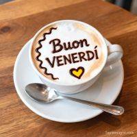 Tazza di cappuccino con schiuma decorata con la scritta “Buon venerdì” e un cuore su un tavolo di legno